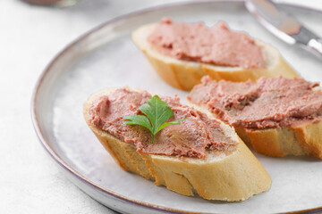 Obraz na płótnie Canvas Homemade chicken liver pate on fresh french white wheat baguette slices on wooden plate, glass mason jars with cooked liverwurst, top view