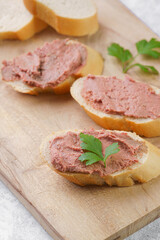 Homemade chicken liver pate on fresh french white wheat baguette slices on wooden plate, glass mason jars with cooked liverwurst, top view