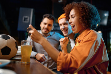Cheerful friends having fun watching football game on smartphone at sport bar