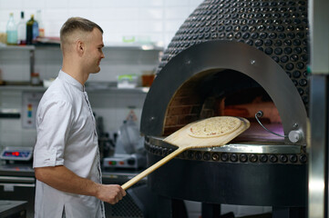 Professional baker chef making traditional italian pizza in oven