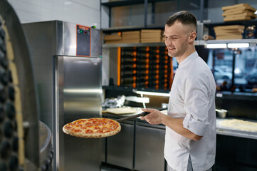 Cheerful young man working in pizza shop presenting fresh baked pastry