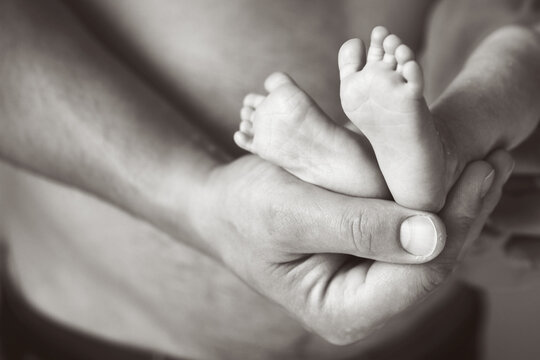 Father holding newborn baby feet on his hands