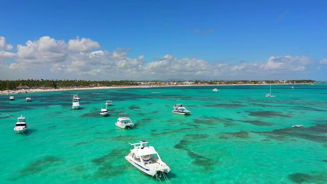Aerial flight above white anchoring yachts and tourist boats in the turquoise Caribbean sea. Best destination for beach vacation in Punta Cana