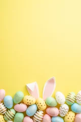 Fotobehang Easter celebration concept. Top view vertical photo of colorful easter eggs and easter bunny ears on isolated yellow background with empty space © ActionGP
