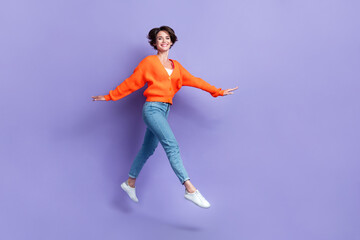 Fototapeta na wymiar Full length photo of careless good mood youngster active girl orange knitwear denim jeans walking flying pleasure isolated on violet color background