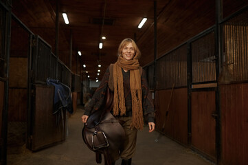 Fototapeta na wymiar Female horse rider walking with harness in stable