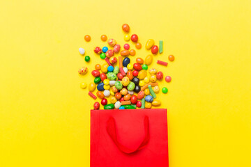 shopping paper gift bag in corner full of assorted traditional candies falling out on colored...