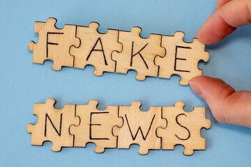 Wooden puzzles with Fake News on a dovish background in a woman's hand. Misinformation, propaganda, clickbait, media literacy.