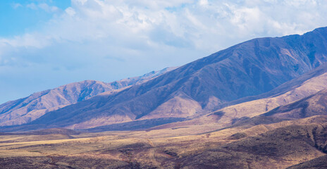 Unusual mountain landscape with bright cloudy skies. Autumn in remote foothills in northern China. Dry grassy and hills. Natural background. Exploration of new places, travel to remote locations.