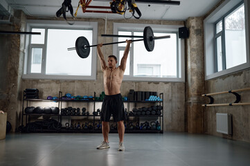 Muscular guy lifting barbell above head standing at gym