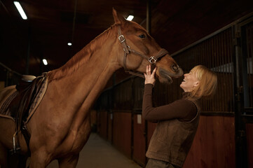 Happy woman laughing while horse kissing her in stable of riding club