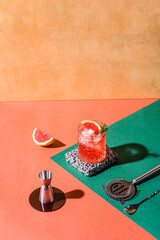 Red cocktail in base of Campari or bitter with blood red oranges (tarocco) on the geometric  background. Aperitif with Americano or Negroni cocktail. Retro chic style. Barmans tools and props