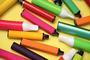 Set of multicolor disposable electronic cigarettes on a bright yellow background.