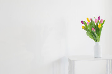 tulips in white vase on wooden shelf on white background
