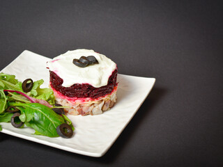 Top view of Norwegian layered fish salad Herring under fur coat. Portion with marinated herring, onion, grated potato, beetroot, mayonnaise on top with lettuce olive salad. Dark copy space background