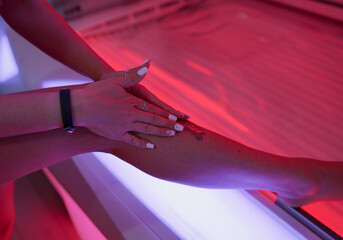A girl applies sunscreen to her body in a solarium, close-up photo.