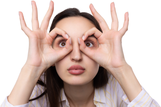 Close up portrait of attractive quirky young woman making binoculars with hands showing ok gesture on white studio background.