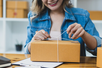 Small startup business concept. Woman tying ropes on a parcel box packs items in preparation for shipping an order. Preparing to ship for e-commerce sellers.
