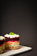 Layered fish salad Herring under fur coat served in culinary rings on dark background. Portion of salad with marinated herring, onion, grated potato, beetroot, mayonnaise on top. Vertical image