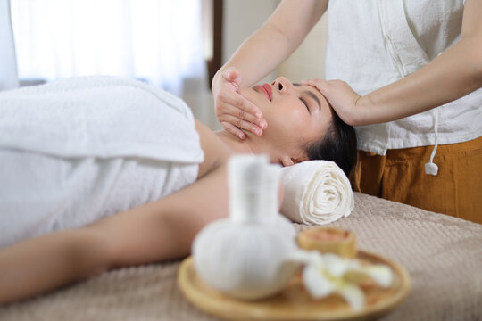 Relaxed Asian woman receiving beauty massage in spa salon.