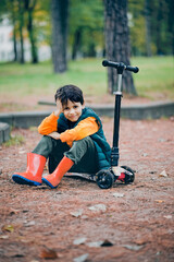 Cute little boy sitting on a scooter in the park in the fall.