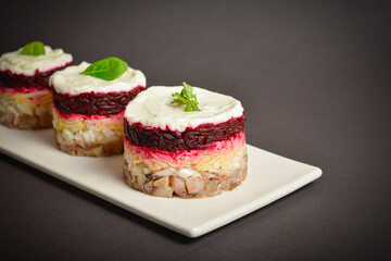 Side view of holiday layered fish salad Herring under fur coat served in culinary rings. serving size of Eastern Europe salad with beetroot, potato, onion, fish and mayonnaise with towel on background