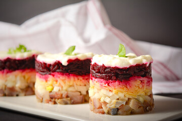 Macro shot of layered fish salad Herring under fur coat served in culinary rings. Salad portion with marinated herring, onion, grated potato, beetroot, mayonnaise on top. Kitchen towel on background