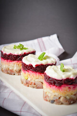 Side view of layered fish salad Herring under fur coat served in culinary rings. Portion of salad with marinated herring, onion, grated potato, beetroot, mayonnaise on top. Kitchen towel on background