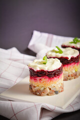 Traditional holiday layered fish salad Herring under fur coat served in culinary rings. serving size of Eastern Europe salad with beetroot, potato, onion, fish and mayonnaise with towel on background