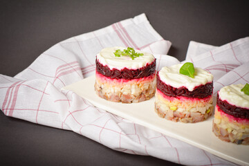 Traditional holiday layered fish salad Herring under fur coat served in culinary rings. serving size of Eastern Europe salad with beetroot, potato, onion, fish and mayonnaise with towel on background