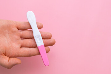 Man hand holding a pregnancy test on the pink background with copy space