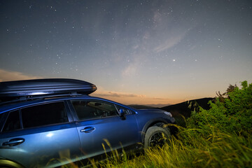 Fototapeta na wymiar Blue offroad SUV car with roof trunk on background of very beautiful night starry sky after sunset. Freedom and travel by car concept