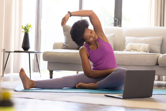 Mid adult african american woman practicing online yoga in living room at home