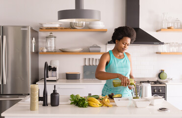 Mid adult african american woman preparing healthy juice in kitchen at home