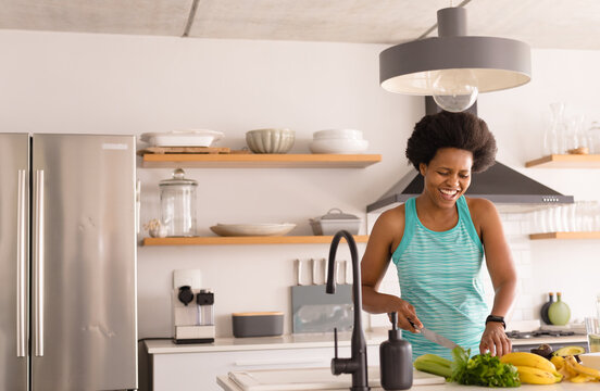 Happy Mid Adult African American Woman Chopping Vegetables In Kitchen At Home