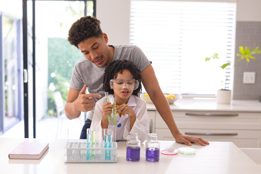 Hispanic father guiding son doing science research with chemical solutions at home