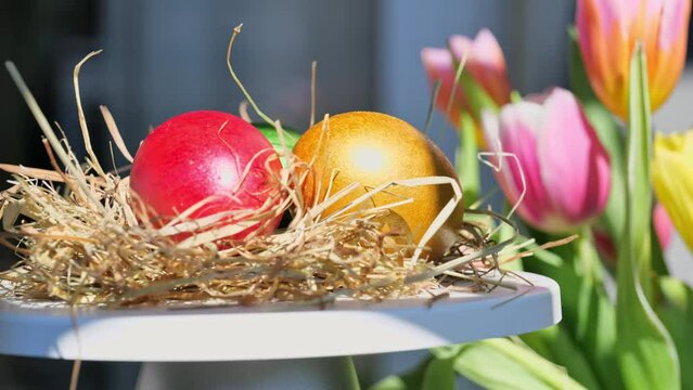 Easter colorful eggs rotate in nest in hey outdoor in sunny warming day, tulips flower background. Happy Easter holiday. Christian celebration, family traditions. Selective focus