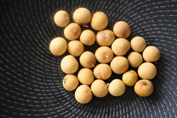 top down many yellow longan fruit on black plate 