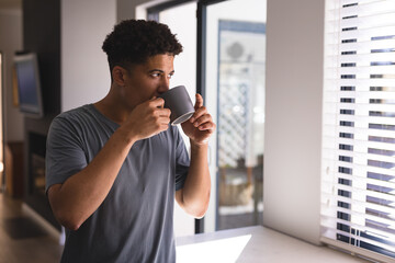 Hispanic man drinking coffee while standing at home looking away