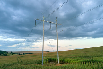 Fototapeta premium High voltage tower with electric power lines between green agricultural fields. Transfer of electricity concept