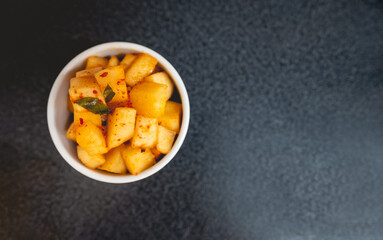 Spicy traditional turnip kimchi in white bowl in table in kitchen with big copy space (kimchi: pickled and fermented vegetables, garlic, salt, ginger, chili peppers, etc)