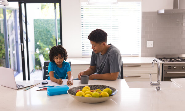 Hispanic man sitting by son doing homework at kitchen island