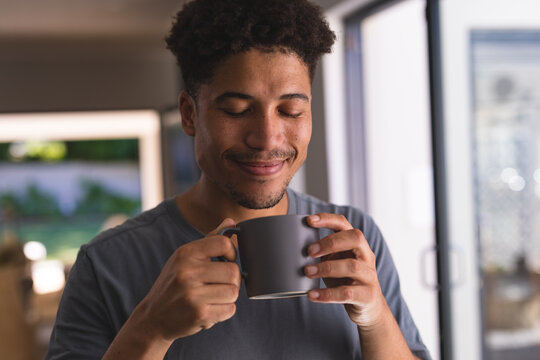 Smiling hispanic man with eyes closed holding coffee mug at home