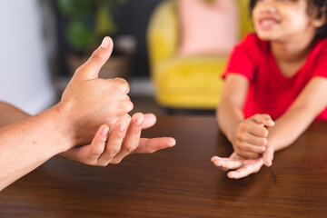 Hispanic father and son talking through hand sign language while sitting at dining table