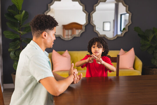 Hispanic boy learning sign language from father while sitting at dining table - Powered by Adobe