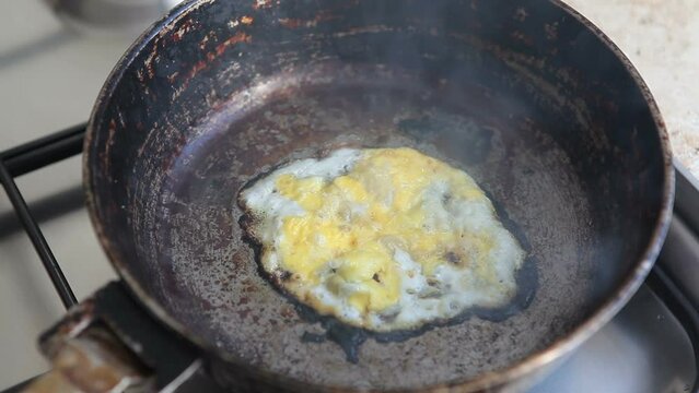 Forgotten scrambled eggs are burning in an old frying pan. A chicken egg burned on a gas stove.