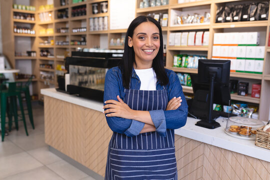 Portrait of smiling young female caucasian barista with arms crossed standing at coffee shop