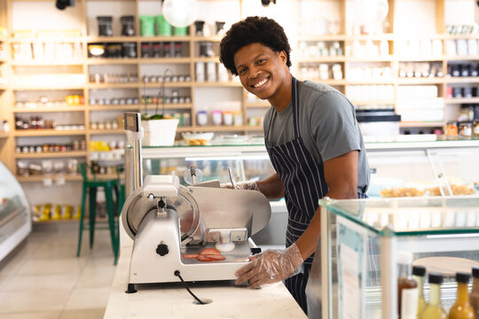 Portrait Of Smiling Young Male African American Employee Using Meat Slicer At Counter In Coffee Shop