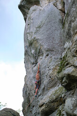 Strong male climber climbing steep wall of rocky mountain. Sportsman overcoming difficult route. Engaging in extreme sports hobby concept