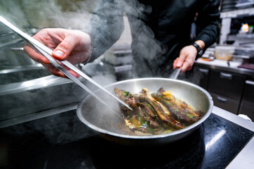 man chef cooking fried meat slice in frying pan on restaurant kitchen